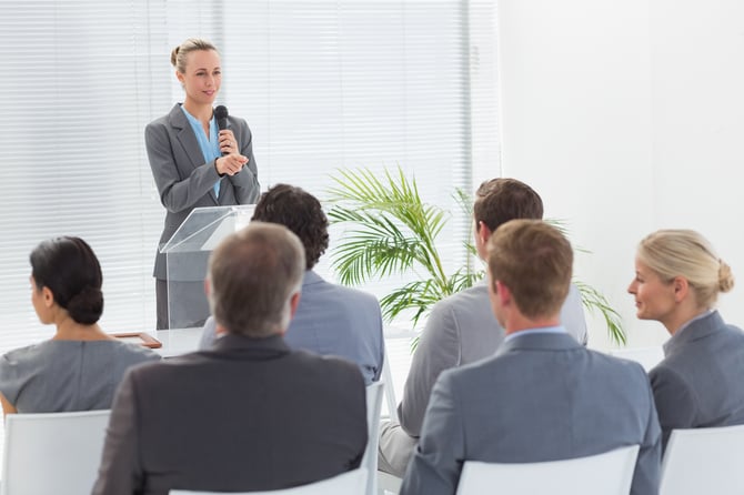 Pretty businesswoman talking in microphone during conference in meeting room